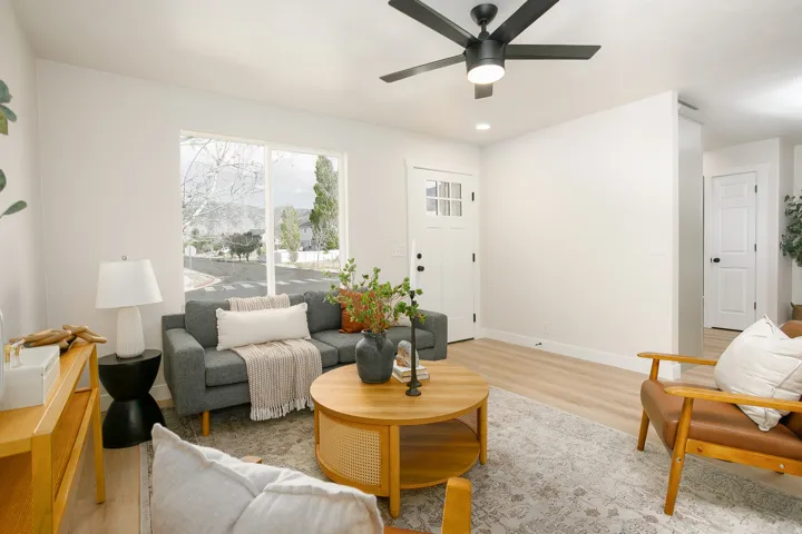 Bright living area featuring light wood-finish flooring, a contemporary ceiling fan, and a white paneled entry door with windowpanes
