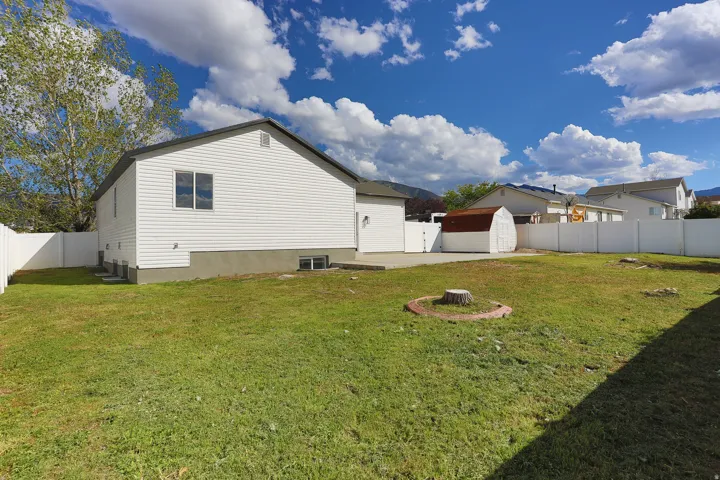 Expansive fenced yard featuring a concrete patio, a storage shed, and mature trees