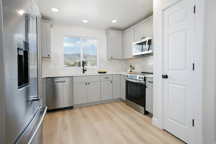 Modern kitchen featuring light wood-finish flooring, stainless steel appliances, light gray cabinetry, and white countertops