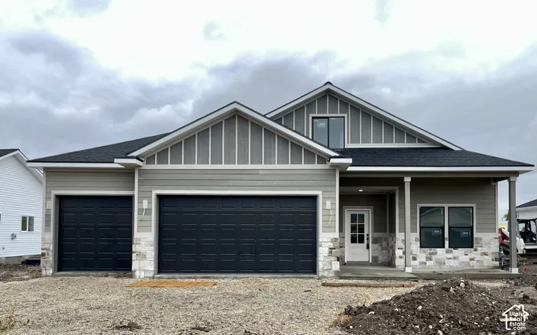 Exterior featuring horizontal lap siding, vertical board-and-batten gable accents, stone veneer foundation, asphalt shingle roof, and a three-car garage