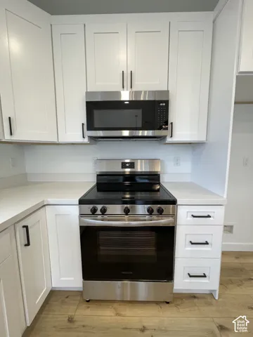 Kitchen featuring white shaker-style cabinetry, solid-surface countertops, wood-finish flooring, and stainless steel appliances including a built-in microwave and range