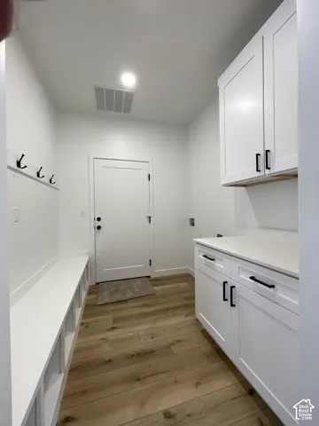 Utility room featuring white cabinetry, a solid surface countertop, built-in lower cubbies with a bench seat, wall-mounted hooks, and wood-finish flooring