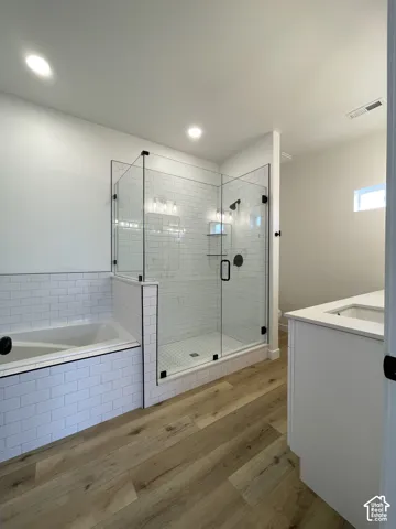 Primary Bath Featuring enclosed glass shower with subway tile surround, deep soaking tub featuring matching tile decking, wood-finish flooring, and white vanity cabinetry with a stone countertop