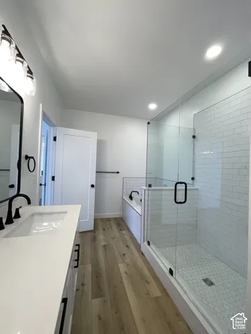 Primary Bathroom featuring a white vanity with a rectangular sink, wood-finish flooring, a glass-enclosed shower with white subway tile, and a soaking tub with matte black hardware