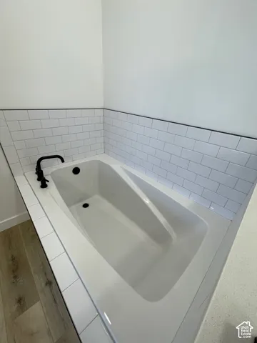 Primary Bath Built-in drop-in bathtub with a white subway tile surround, matte black deck-mounted faucet, and wood-finish flooring