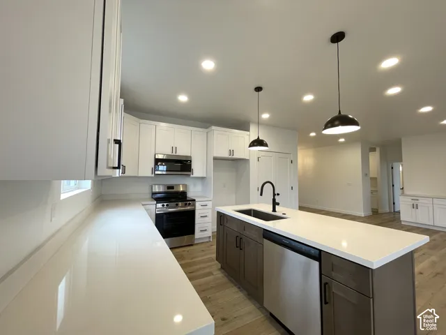 Kitchen featuring white shaker cabinetry, wood-finish flooring, a central island with a contrasting base, quartz countertops, stainless built in dishwasher and matte black hardware