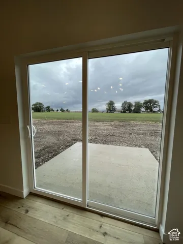 Sliding glass door with white frame, wood-finish flooring, and concrete patio leading to an open landscape
