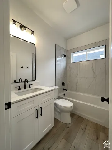 Main Bathroom featuring a white vanity cabinet with quartz countertop, undermount sink, matte black hardware, tiled tub surround, and wood-finish flooring