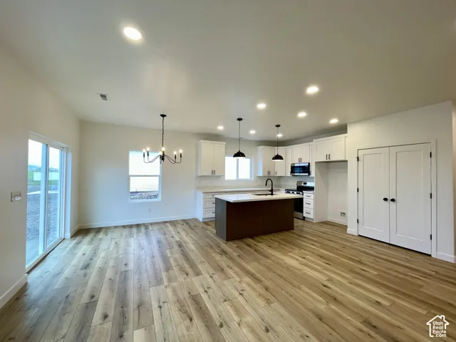 Open-concept area featuring wood-finish flooring, a kitchen island with stone-surface countertop, recessed lighting, double-door pantry, and sliding glass door