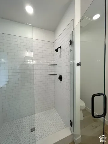 Primary Bath Walk-in shower with white subway tile walls, hexagonal floor tile, matte black fixtures, integrated glass shelving, and a frameless glass door