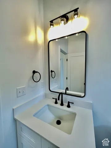 Vanity featuring a white countertop with an integrated basin, matte black widespread faucet, rectangular mirror with a black frame, and a three-light vanity fixture