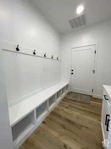 Built-in mudroom cabinetry featuring integrated cubby storage, wood-finish flooring, white shaker-style door, and matte black hardware