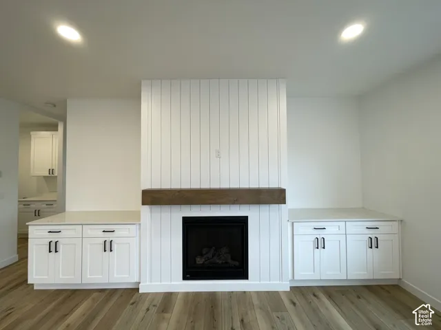 Fireplace feature wall with white vertical plank detailing, stained wood mantel, built-in lower cabinetry with light-colored countertops, and matte black hardware, set above wood-finish flooring
