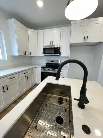 Kitchen featuring white shaker-style cabinetry, quartz countertops, a stainless steel undermount sink with a matte black high-arc faucet, and stainless steel appliances