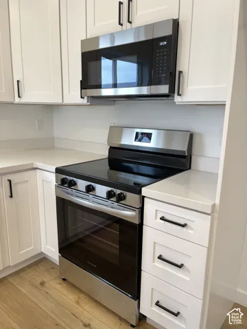 White shaker-style cabinetry with matte black hardware, stainless steel over-the-range microwave, stainless steel slide-in range, solid surface countertops, and wood-finish flooring