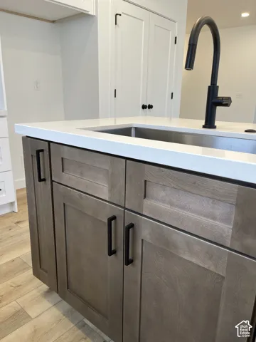Kitchen island featuring custom-finish cabinetry, matte black hardware, white solid-surface countertops, an undermount stainless steel sink, a matte black high-arch pull out sprayer faucet.