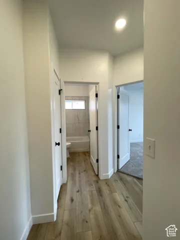 Hallway featuring wood-finish flooring, white solid-core doors with matte black hardware, and recessed lighting