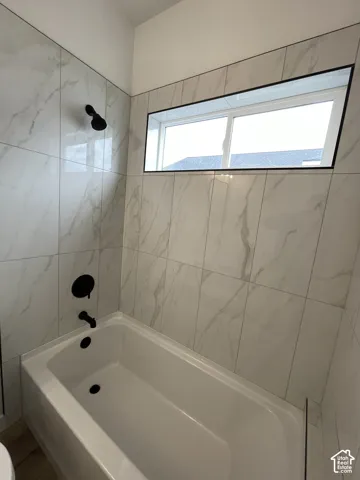 Full-height tile surround with a white stone-patterned finish, white acrylic bathtub, matte black plumbing fixtures, and a horizontal sliding window