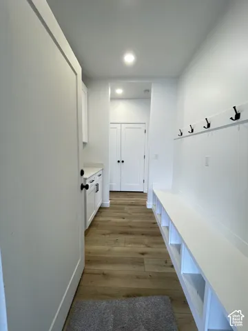 Built-in bench with lower shelving, integrated coat hooks, wood-finish flooring, white cabinetry, and recessed lighting