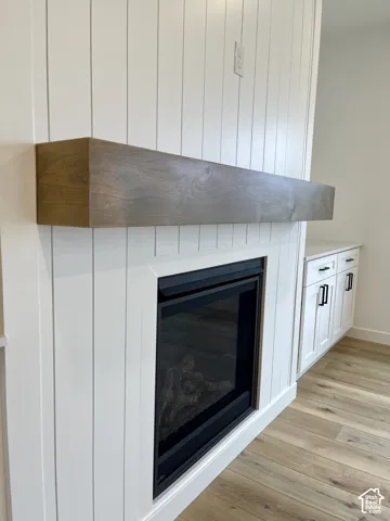 Gas Fireplace featuring a vertical plank surround, stained wood mantel, and built-in white cabinetry with matte black hardware over wood-finish flooring