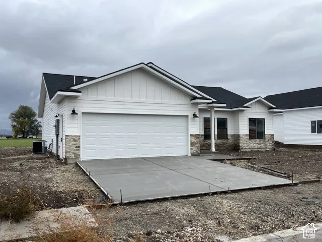 Exterior featuring horizontal siding, stone veneer base, a dark asphalt shingle roof, dual garage door, and metal exterior light fixtures