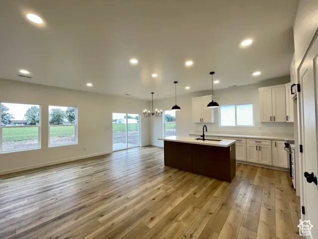 Open-concept kitchen and living area featuring wood-finish flooring, recessed lighting, a kitchen island with a dark finish, white cabinetry, and sliding glass doors