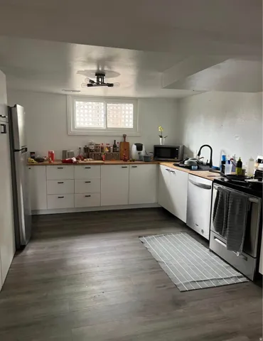L-shaped kitchen with wood-finish countertops, white cabinetry with dark hardware, stainless steel appliances, and wood-finish flooring