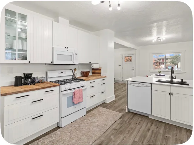 White cabinetry, wood-finish countertops, stainless steel appliances, and wood-finish flooring