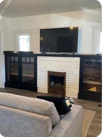 White brick fireplace with an ornate metal grate, flanked by custom built-in cabinetry with glass panel doors, and wood-finish flooring