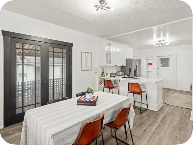 Dining area featuring dark-framed glass paneled doors, wood-finish flooring, and a kitchen with white cabinetry, a built-in refrigerator, and a kitchen island with seating