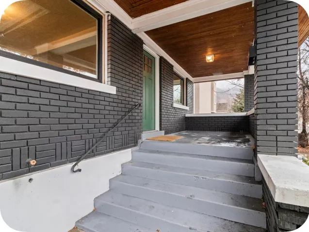 Covered front porch featuring a wood-finish ceiling, dark brick exterior, and a green entry door