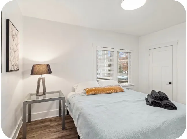 Recessed lighting, wood-finish flooring, white paneled door with matte black hardware, and an egress window with blinds