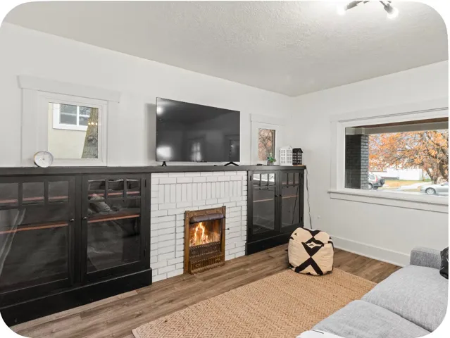 White brick fireplace with an ornate metal insert, flanked by built-in cabinetry with glass doors, wood-finish flooring, and white trim