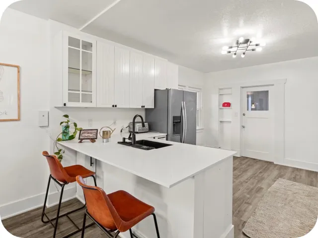 White shaker cabinetry, built-in shelving, white quartz countertops, stainless steel appliances, and wood-finish flooring