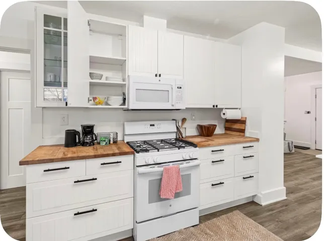 White cabinetry with black hardware, wood-finish countertops, stainless steel gas range, and wood-finish flooring