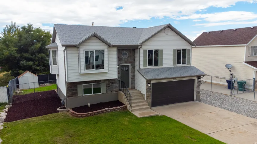 White siding exterior with stone accents, a two-car garage, concrete driveway, and a front entry with handrails