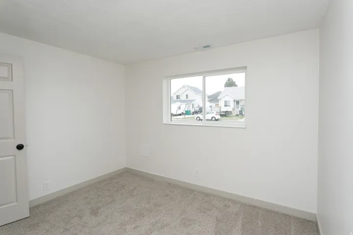 White interior walls, gray carpeting, white trim, and a white interior door with a dark knob