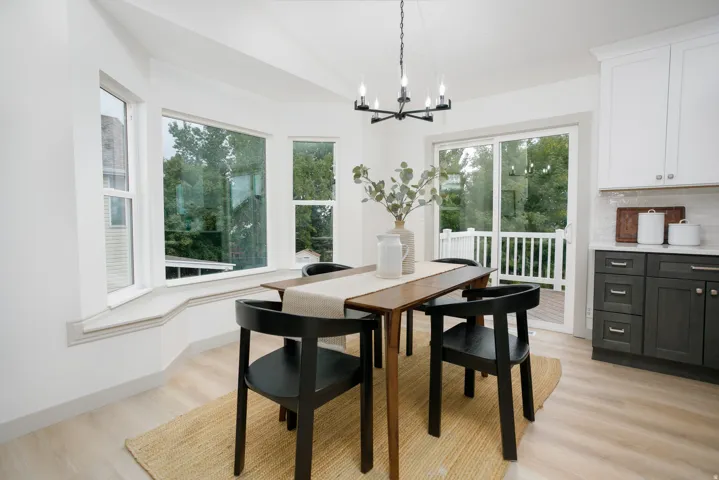 Bay window with a window seat, light wood-finish flooring, sliding glass door, two-tone cabinetry, and a contemporary chandelier