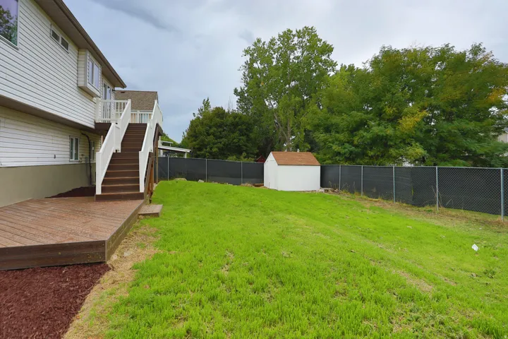 Expansive backyard featuring a manicured lawn, a white storage shed, and a privacy fence