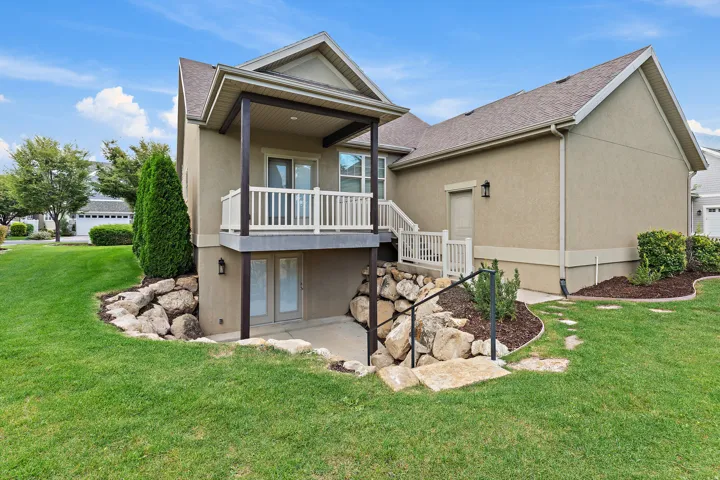 Stucco exterior with a covered balcony, French doors, and mature landscaping