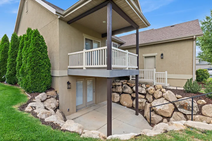 Exterior featuring a covered upper-level balcony, a lower-level concrete patio, and a stone retaining wall