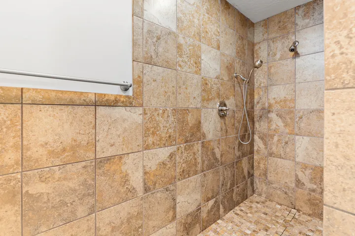 Tiled shower enclosure featuring a fixed shower head and a handheld shower wand