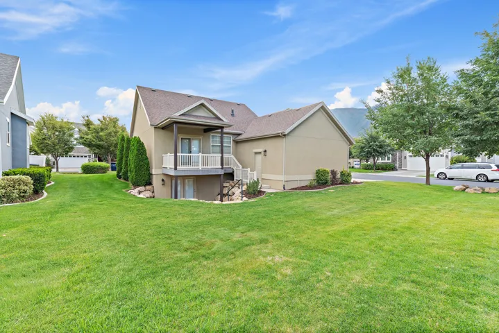 Expansive backyard featuring a manicured lawn, established landscaping, and a covered balcony with white railings