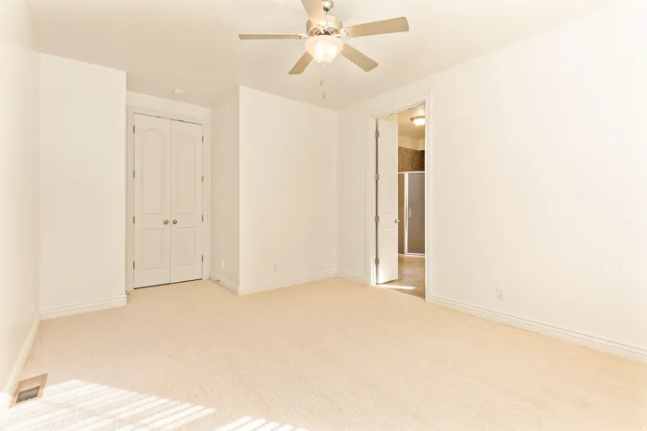 Neutral tone carpeted flooring, white walls, ceiling fan with integrated lighting, double bi-fold closet doors, and an open doorway