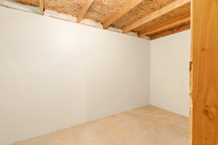 Unfinished space with a concrete floor, light-toned walls, exposed wood ceiling joists, and visible insulation