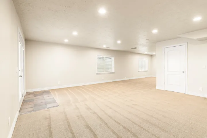 Expansive room featuring recessed lighting, light-colored carpet, multiple windows with blinds, and a white paneled door