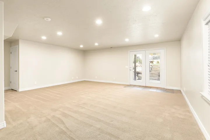 Recessed lighting illuminates this expansive room with neutral wall tones, carpeted flooring, and white trim