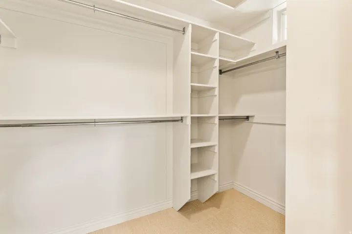 Walk-in closet featuring built-in shelving, multiple hanging rods, and neutral carpet flooring
