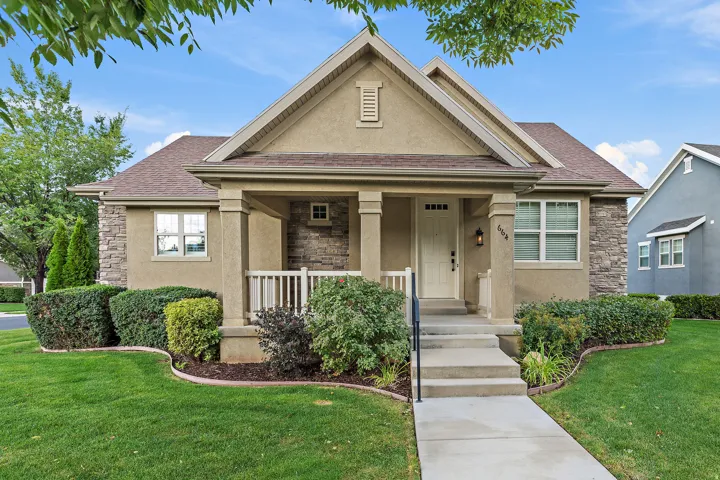 Stucco exterior featuring stone accents, a covered front porch, a gabled roofline, and established landscaping