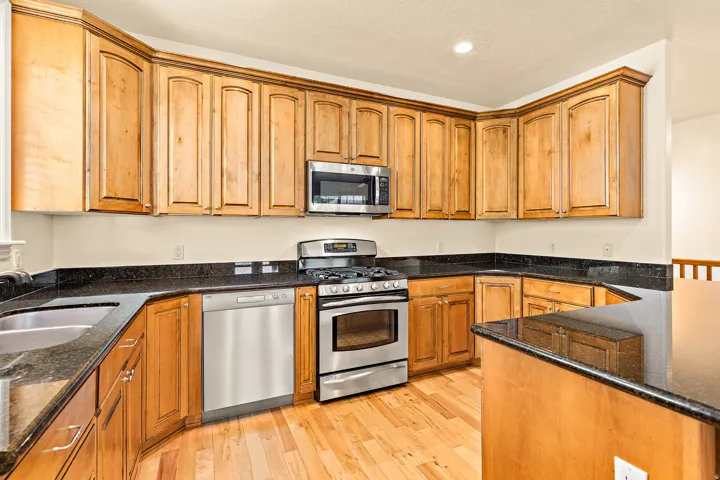 U-shaped kitchen featuring wood cabinetry, dark countertops, stainless steel appliances, and wood-finish flooring